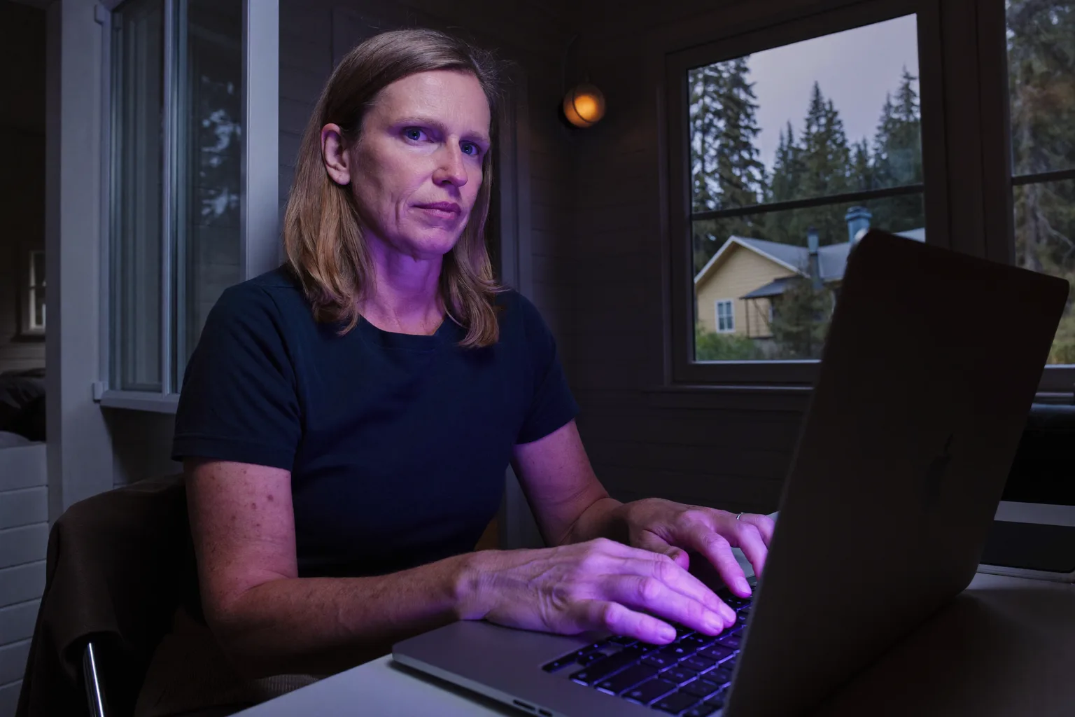 En person som sitter vid ett hemmakontor sent på kvällen och stirrar rakt igenom den bärbara datorns skärm med händerna kvar på tangentbordet, bilden av den tomma tröttheten som hör ihop med utmattningssyndrom på jobbet