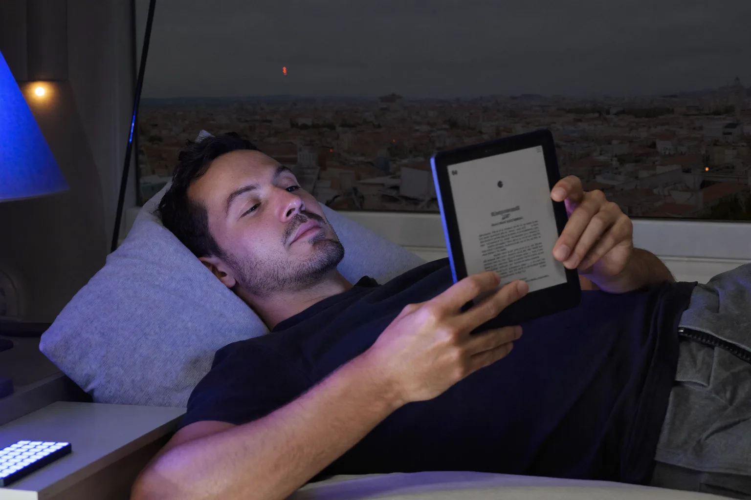 Gece geç saatte yatakta bir e-kitap okuyucudan okuyan bir adam, sayfanın yüzüne zar zor ulaşan sönük bir ışıltı saçtığı bir sahne, yanı başındaki komodinde ekranı yukarı dönük duran bir telefonsa ikinci abajurun gölgeliğini sert ve soğuk bir mavi ışıkla dolduruyor