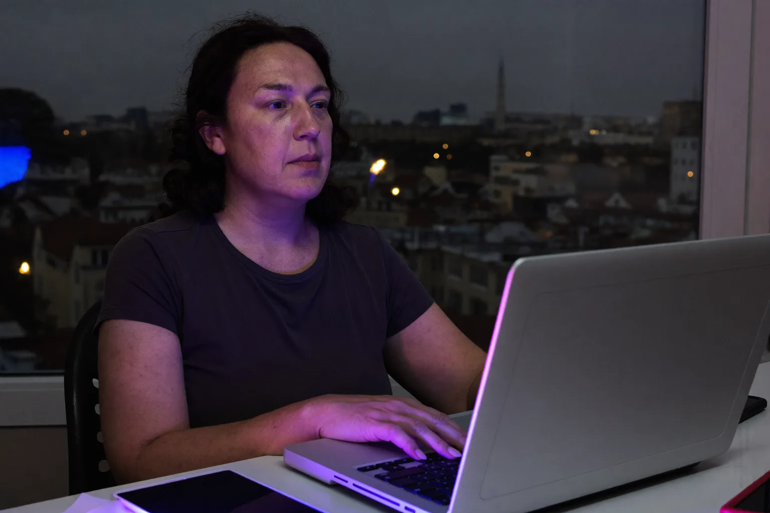 Akşamın geç saatinde ev ofisindeki masasında oturan, elleri hâlâ klavyede dururken laptop ekranının ötesine bakan bir kişi, iş yerinde tükenmişliğin donuk bitkinliğini gösteriyor