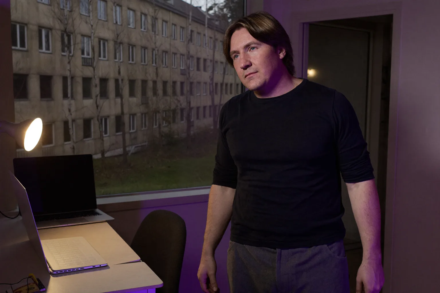 Закритий ноутбук на домашньому столі увечері, у кімнаті горить світло, а людина йде геть, символізуючи кінець робочого дня на віддаленій роботі