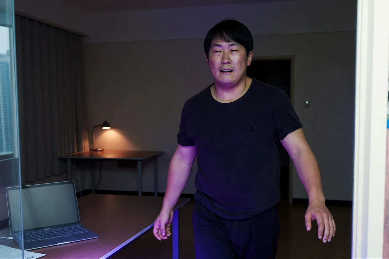 晚上，家里书桌上的笔记本电脑合上了，房间灯还亮着，一个人正转身走开，象征居家办公这一天的结束