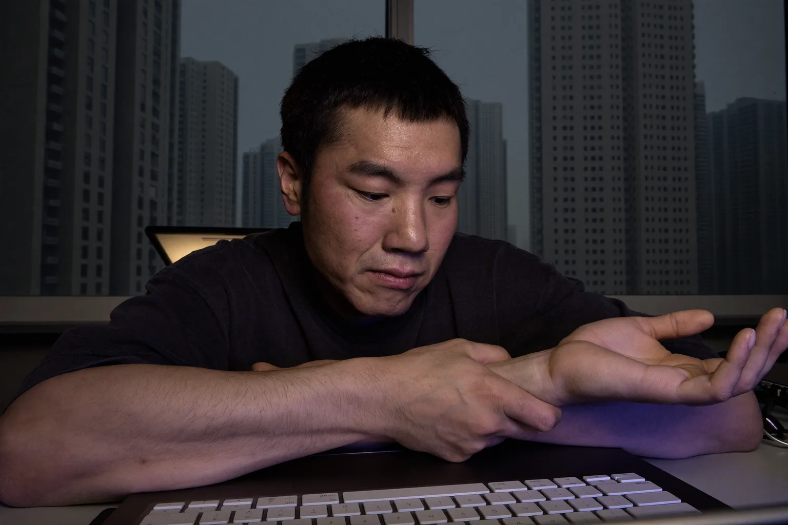 一个人坐在书桌前，用左手握着自己的右手腕，面前放着键盘，画面呈现的是腕管综合征那种又麻又酸的手部感觉