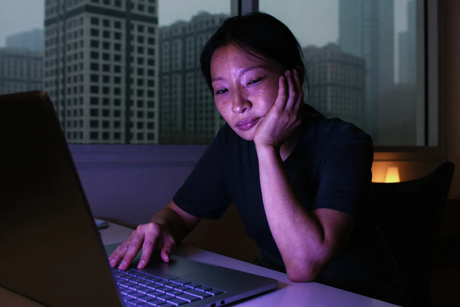 一个疲惫的女人深夜还在用笔记本电脑，一只手托着头，眼睛发沉发干，有黑眼圈，房间光线昏暗