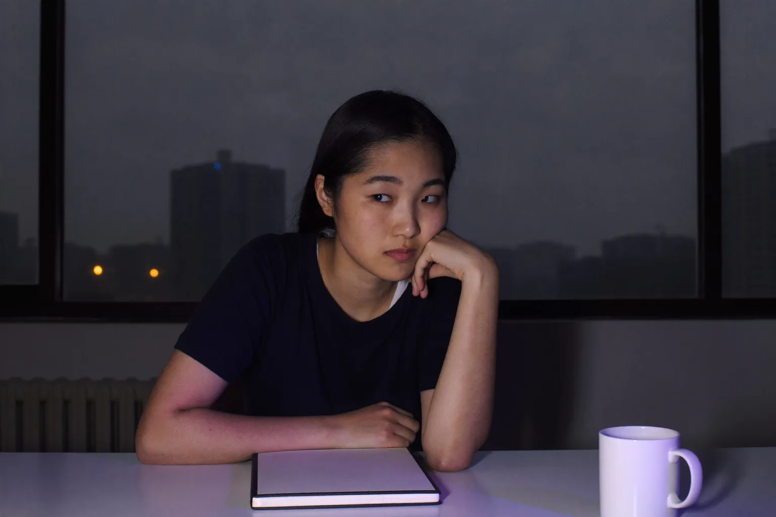 深夜書桌前的學生，手掌托著下巴，臉的一側被螢幕的光照亮，視線飄離作業，望向畫面之外