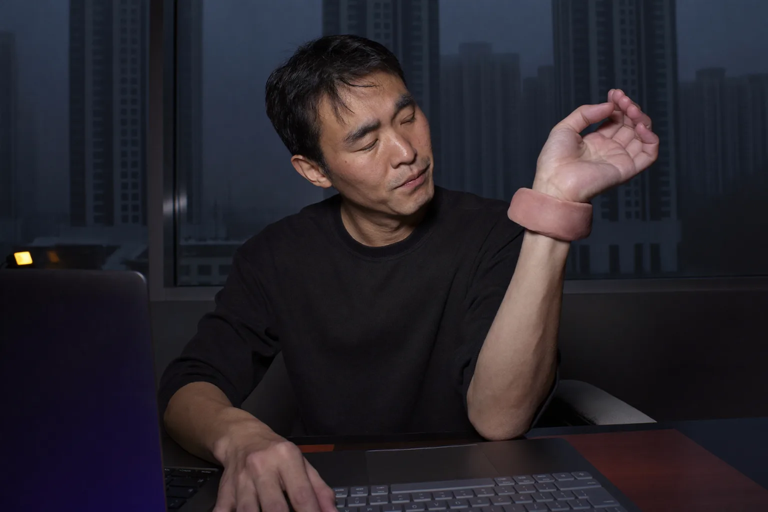 一個人坐在辦公桌前，用另一隻手握著自己的右手腕，前方放著鍵盤，呈現出腕隧道症候群那種又麻又痠的手部感覺